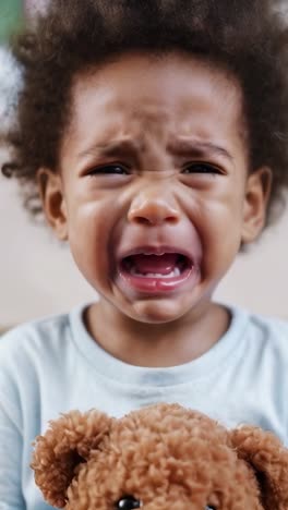 afro little boy crying hugging his teddy bear.