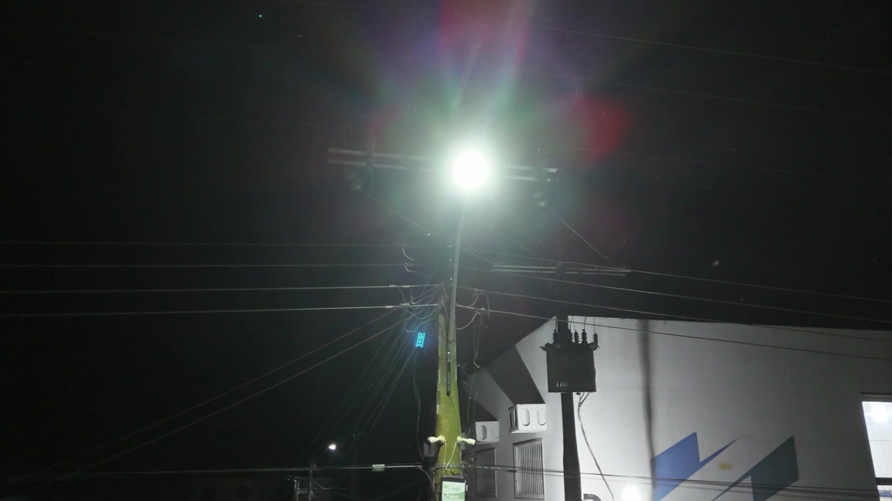 Vista panorámica cinematográfica de una brillante farola montada en un poste de servicios públicos por la noche, iluminando los cables eléctricos aéreos en un entorno urbano