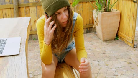 Front-view-of-young-caucasian-woman-with-skateboard-talking-on-mobile-phone-at-outdoor-cafe-4k