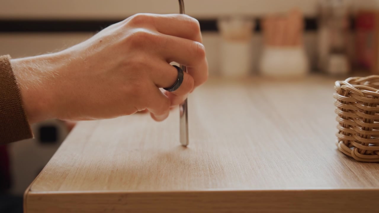 Close up of person hand holding scissors over wooden surface focusing on precise cutting action. Hand with ring moves slightly as scissor blades hover and make contact repeatedly emphasizing