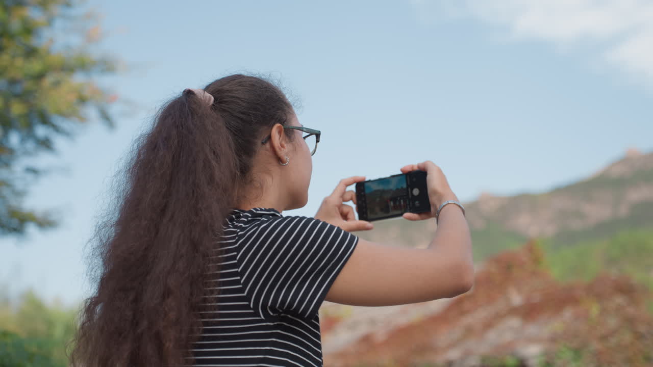 Female traveler viewing mountain temple rooftops from back perspective long curly hair framing serene silhouette, smartphone ready, quiet mood, soft clouds over distant peaks, reflective pause