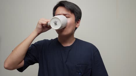 closeup portrait shot southeast asian young man drinks white cup inside room face expression swallowing liquid