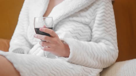 una mujer relajada sosteniendo un vaso de vino rojo vestida con túnica