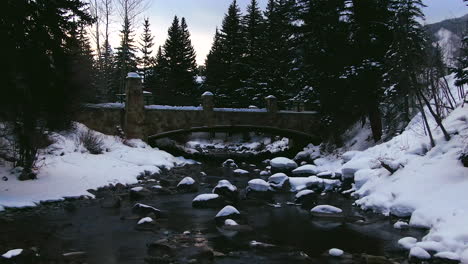 Filmische-Luftdrohne-Den-Gefrorenen,-Verschneiten-Fluss-Am-Frühen-Morgen-In-Der-Innenstadt-Von-Vail-Village-Ski-Resort-Durch-Rückwärtsbewegung-Der-Golden-Peak-Red-Lion-Gondel-Hinunter