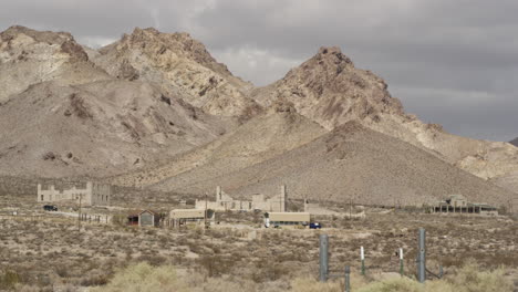 Mining-town-of-Rhyolite,-Nevada-sits-below-the-Desert-mountains-in-the-heat-of-the-summer,-wide