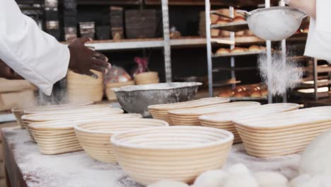 Diverse-bakers-working-in-bakery-kitchen,-pouring-flour-on-baskets-in-slow-motion