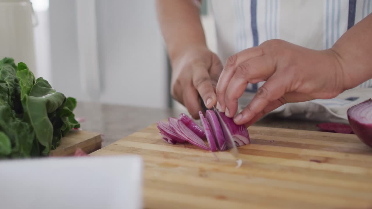 Midsection of african american senior woman preparing food in kitchen, chopping onions