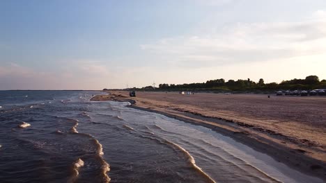 aerial view of a distant garbage truck is loading waste automatically, shifting dumpster on a empty beach coastline, early summer morning after the sunrise, wide angle drone shot moving forward