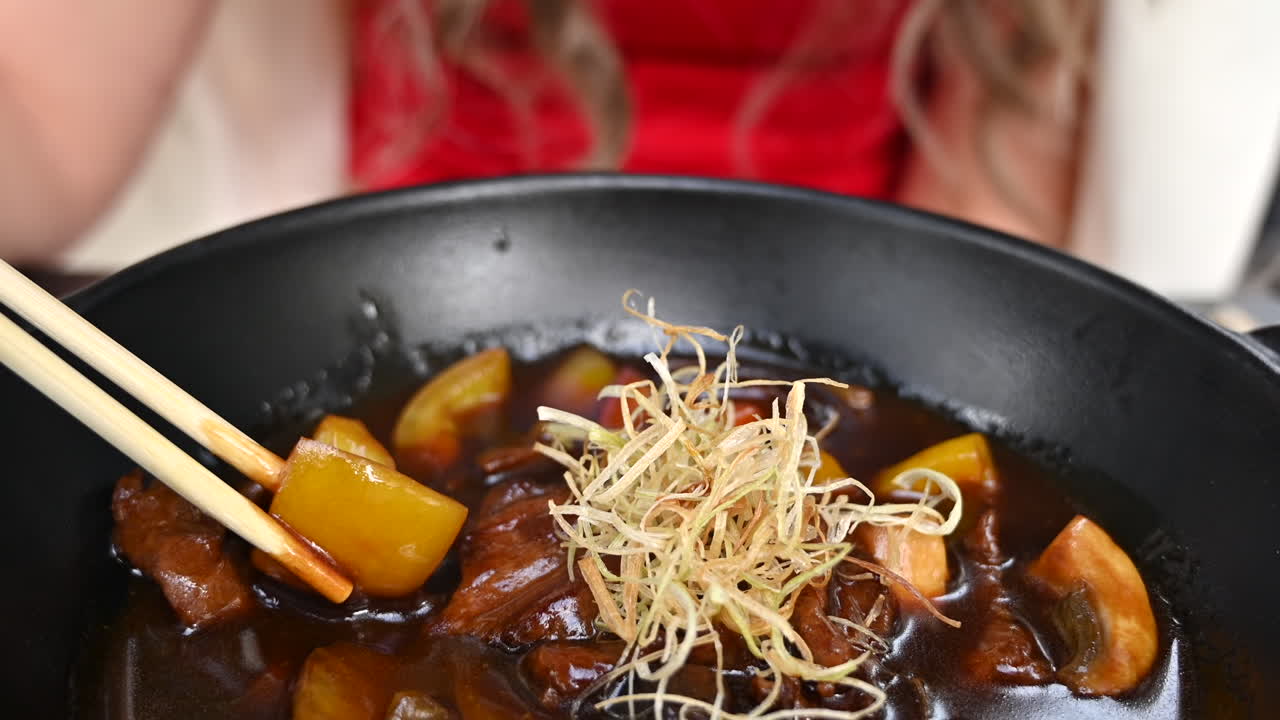 Close up of a woman in a red dress eating beef meat with noodles and vegetables at a Japanese restaurant