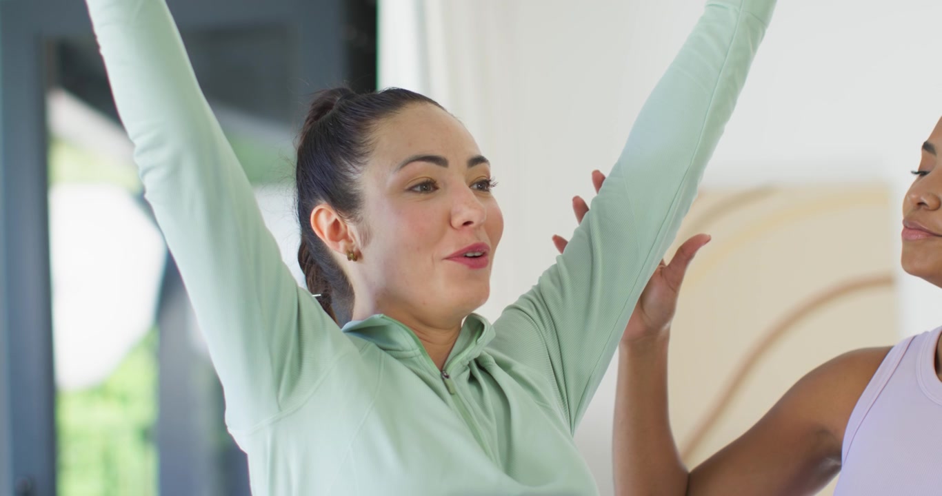 Diverse female friends doing breathwork in bright room assistant placing hand to relax neck