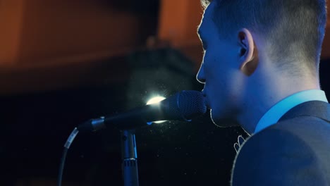 man singing song in microphone during performance on stage on rock concert. close up man rock star singer on music concert on colorful light background