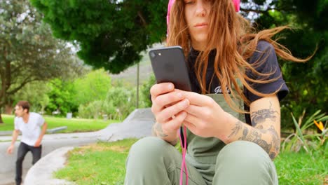 Front-view-of-young-caucasian-woman-listening-music-on-mobile-phone-in-skateboard-park-4k