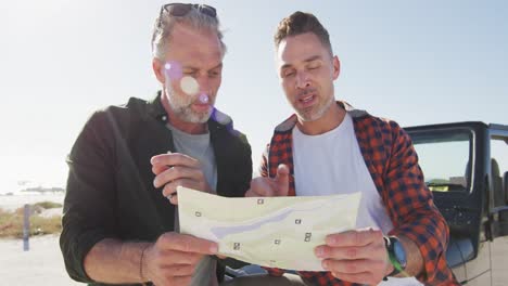 happy caucasian gay male couple by car, reading map and pointing on sunny day at the beach