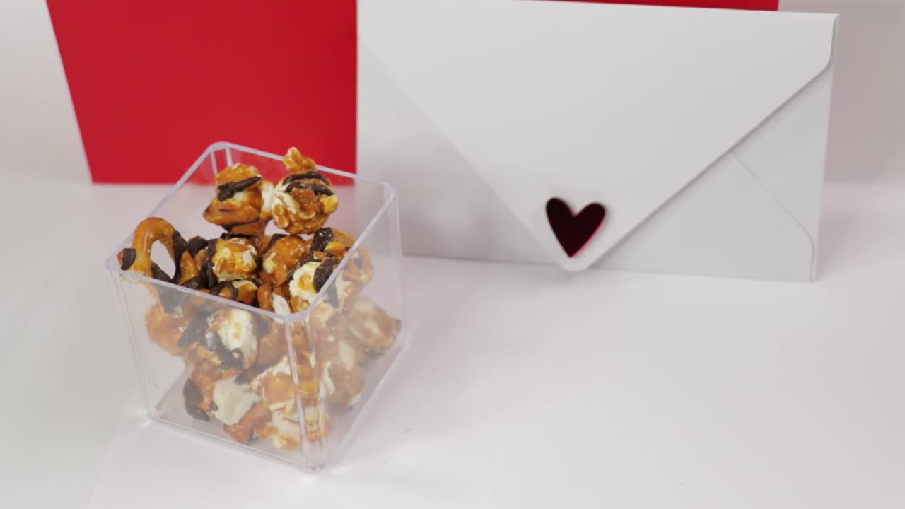 Caramel popcorn and candy falling into plastic box next to love letter