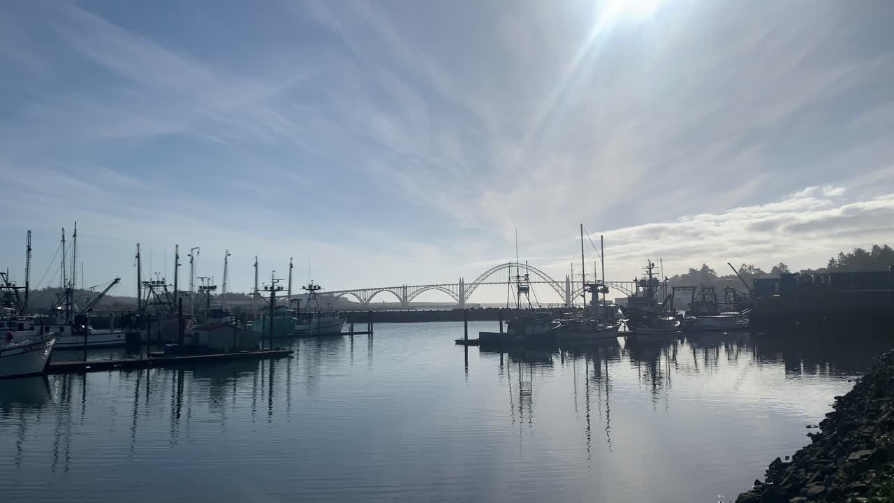 puerto de newport, barcos comerciales flotando en la tranquila bahía con el puente de la bahía de yaquina al fondo en un día soleado