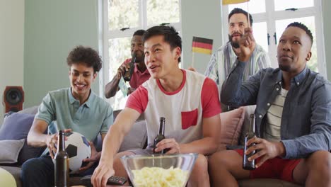 Happy-diverse-male-friends-watching-tv-and-drinking-beer-in-living-room