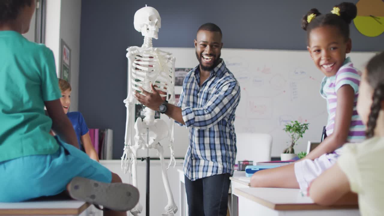 Video of happy african american teacher with class of diverse pupils during anatomy lesson