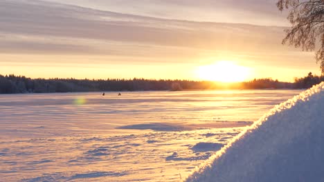 Panning-shot-of-fishermen-on-icy-lake-at-magical-sunrise-in-Lapland,-Finland