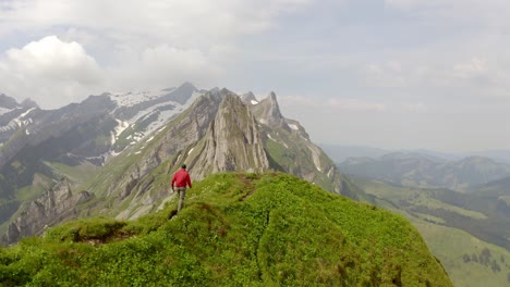 un hombre con una chaqueta roja camina sobre una montaña y es seguido por el dron