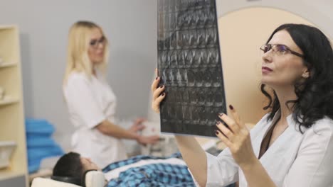 un joven paciente en una mesa automática entra en una máquina de resonancia magnética de tipo cerrado con auriculares de aislamiento de ruido. equipo moderno, bobina en la rodilla del paciente. el médico examina los resultados de la exploración de mri, instantánea