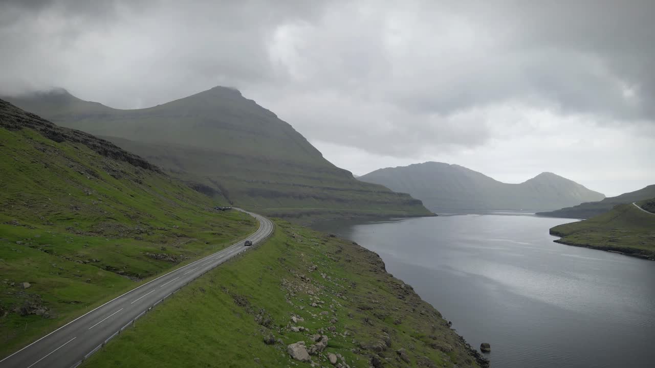 페로 제도의 닝스 (funnings) 에 있는 휘어지는 해안 도로, 푸른 언덕, 거친 절벽, 조용한 물, 그리고 무서운 구름이 가득한 하늘 아래 아오르는 산꼭대기들로 둘러싸여 평온하고 멀리 떨어진 분위기를 만니다.