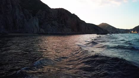 Estela-De-Barco-En-El-Océano-Al-Atardecer-Con-Acantilados-Costeros-En-Segundo-Plano.