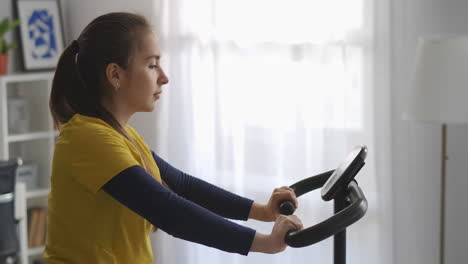 young woman is training with spinning bike in home medium portrait of sporty lady panoramic in living room healthy lifestyle and good physical condition