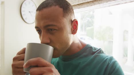Portrait-of-thoughtful-biracial-man-in-kitchen-drinking-coffee