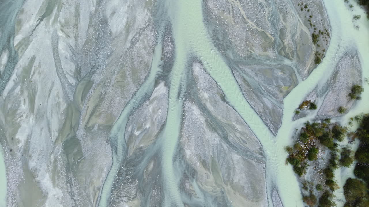 Drone moves forward in full top-down view over frozen braided glacial river and rocky terrain