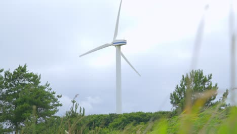 Rear-of-wind-turbine-rotating-on-bright-cloudy-summer-day-with-rise-up-clearing-foreground-grass