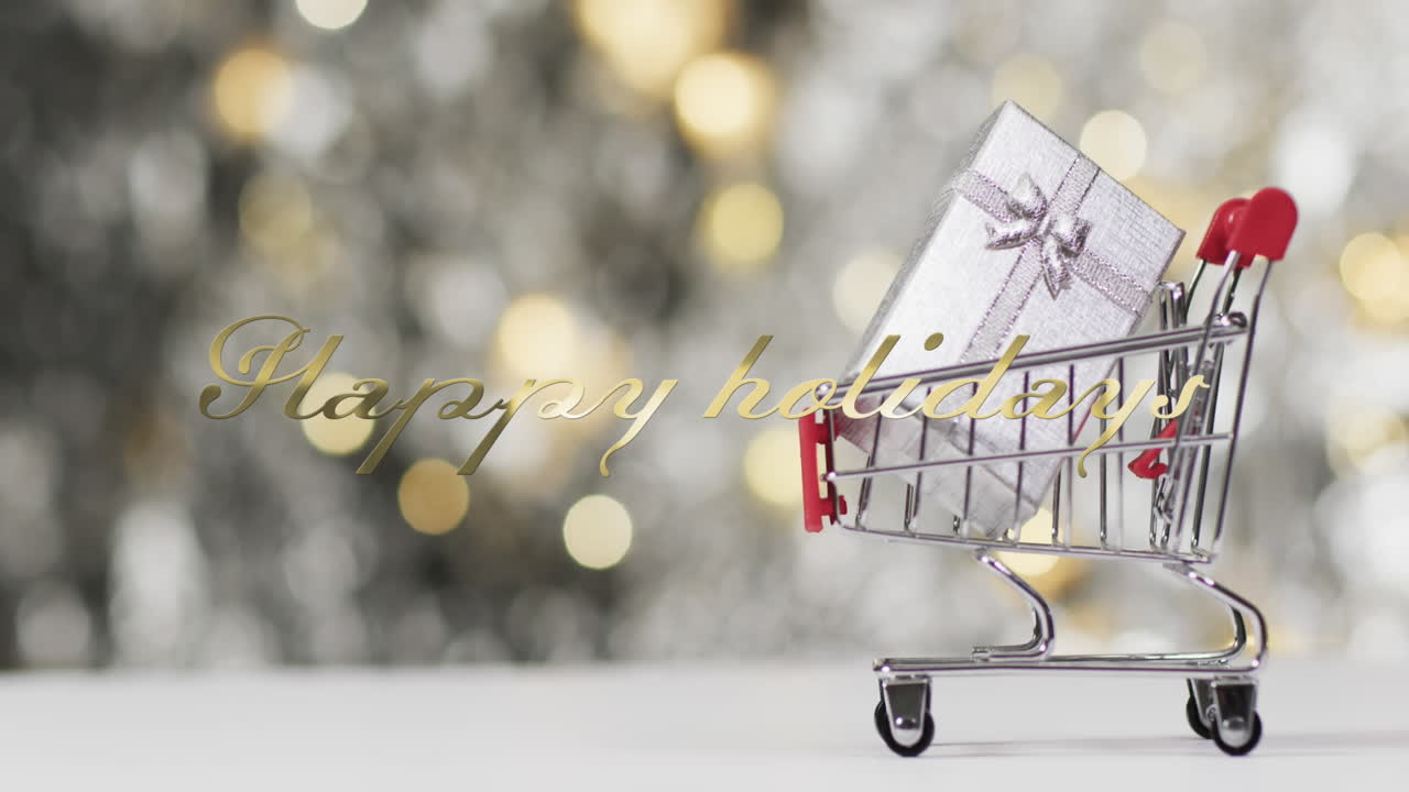 Happy holidays text in gold over christmas gift in shopping cart on bokeh lights background