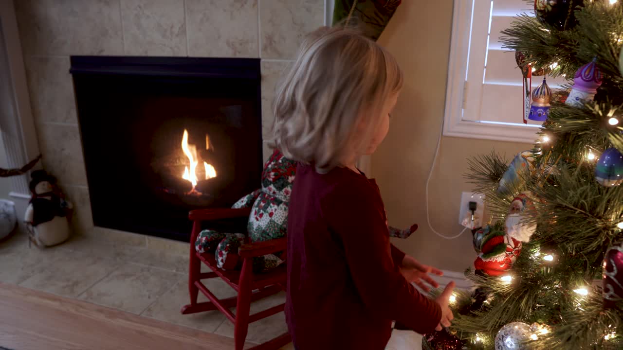 adorable niña de tres años mirando adornos en el árbol de navidad junto a la chimenea