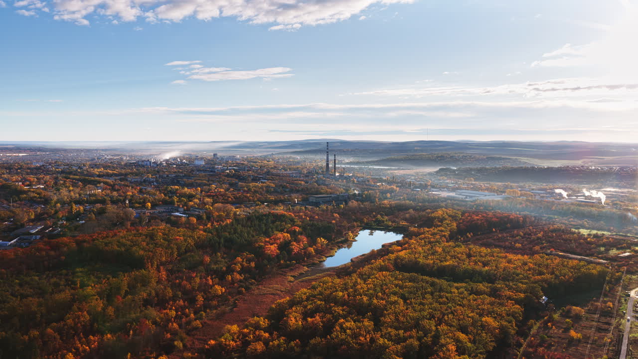 Aerial drone view of a Moldovan city bordered by autumn colored forests and a river, with distant industrial chimneys