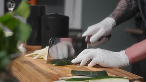 calabacín fresco cortado en una tabla de madera por un joven chef profesional con un elegante pantalones negro con tatuajes