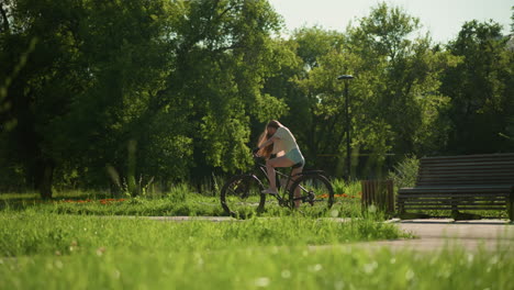 cyclist mounts bicycle near vibrant garden, preparing for ride surrounded by colorful flower beds under warm sunlight, scene includes lush greenery, tall trees, and a wooden bench