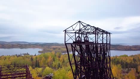 slow-motion aerial-orbit panning shot of an abandoned mine headframe in the boreal forest in the fall with a lake in the background