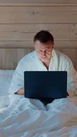 working late at night while wrapped in a cozy blanket and bathrobe in a modern bedroom