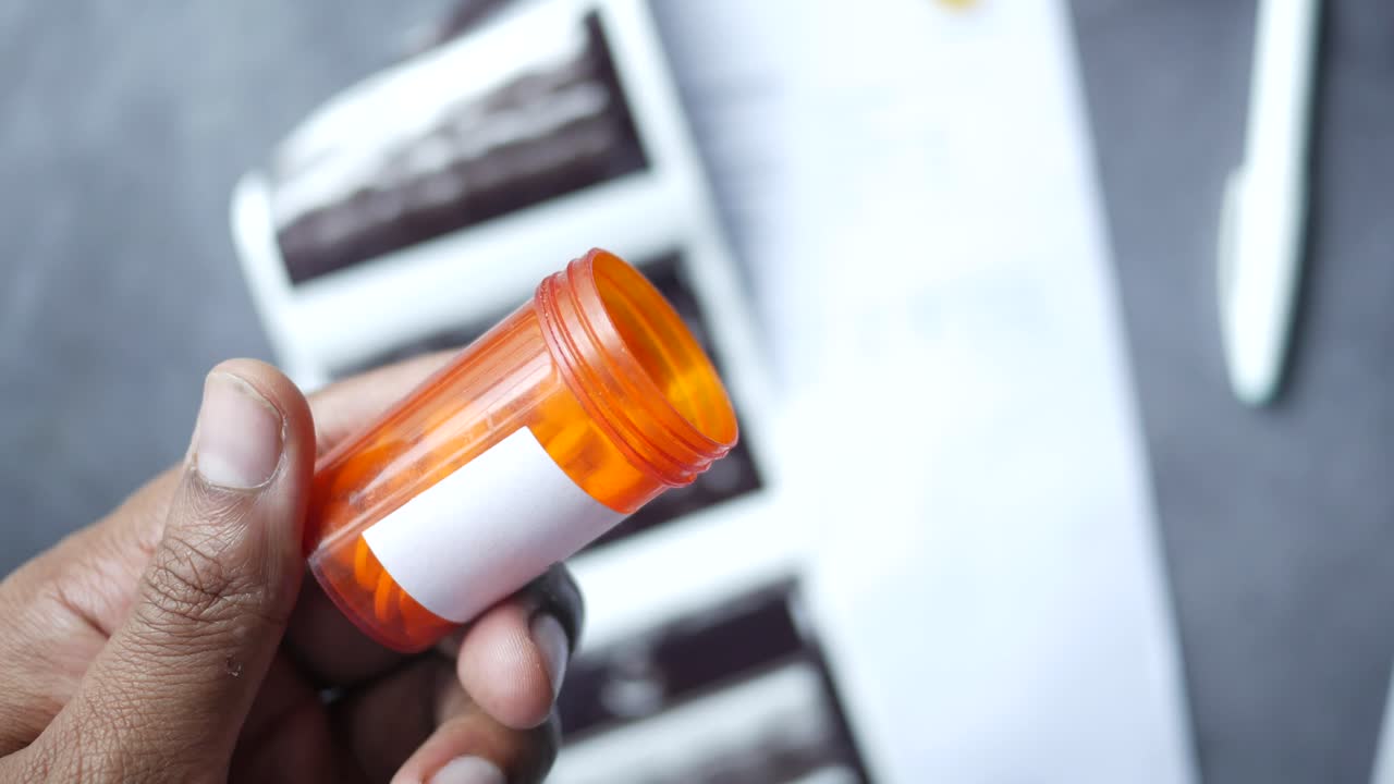mano sosteniendo una botella de pastillas, documentos médicos e imágenes de ultrasonido en el fondo