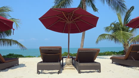 Red-sun-umbrella-and-deckchair-on-white-sandy-beach-with-sea-in-background