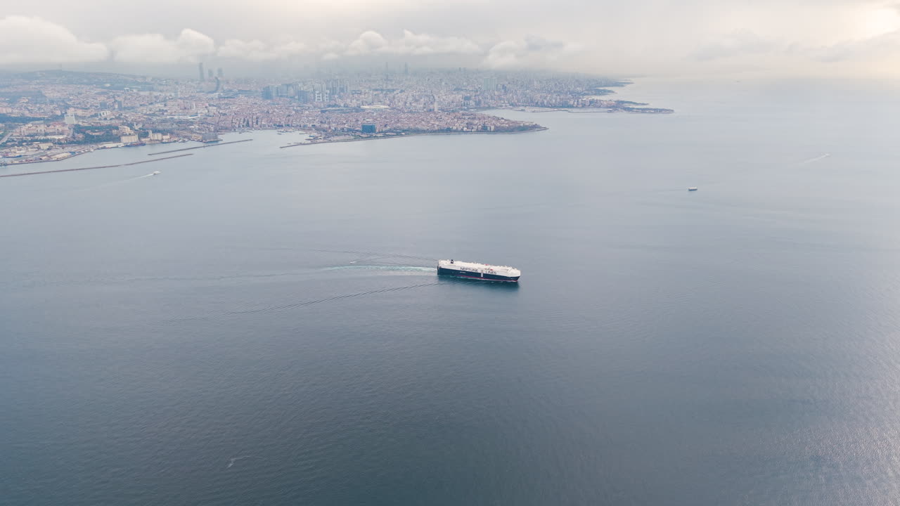 Aerial view of a heavy cargo ship Neptune Lines, sailing through the Bosphorus near Istanbul, with the city skyline in the distance. International shipping over calm sea waters in Turkey. UHD