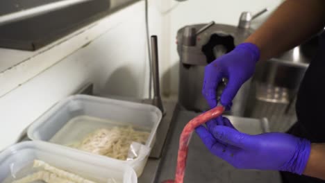 butcher stuffing sausages in industrial kitchen, wearing blue gloves for hygiene