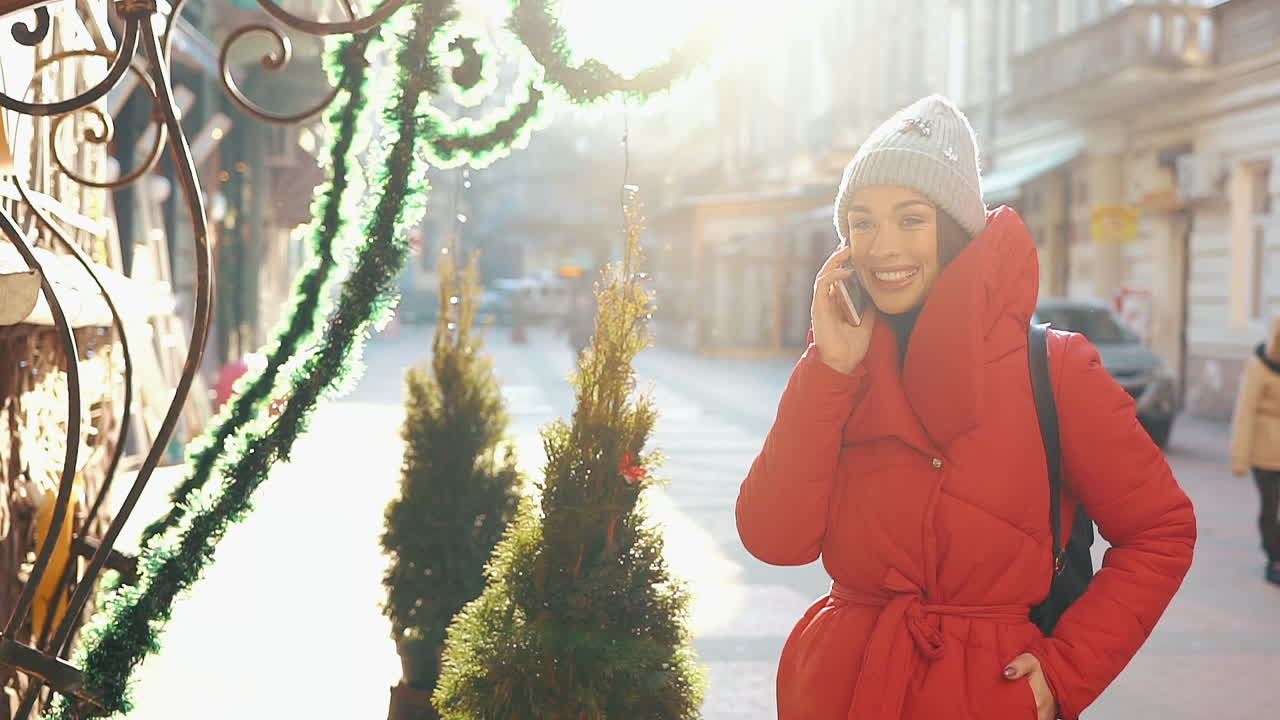Woman in red coat talking on the phone on a city street in winter