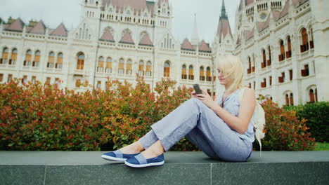 the woman sits on the background of the hungarian parliament uses a smartphone