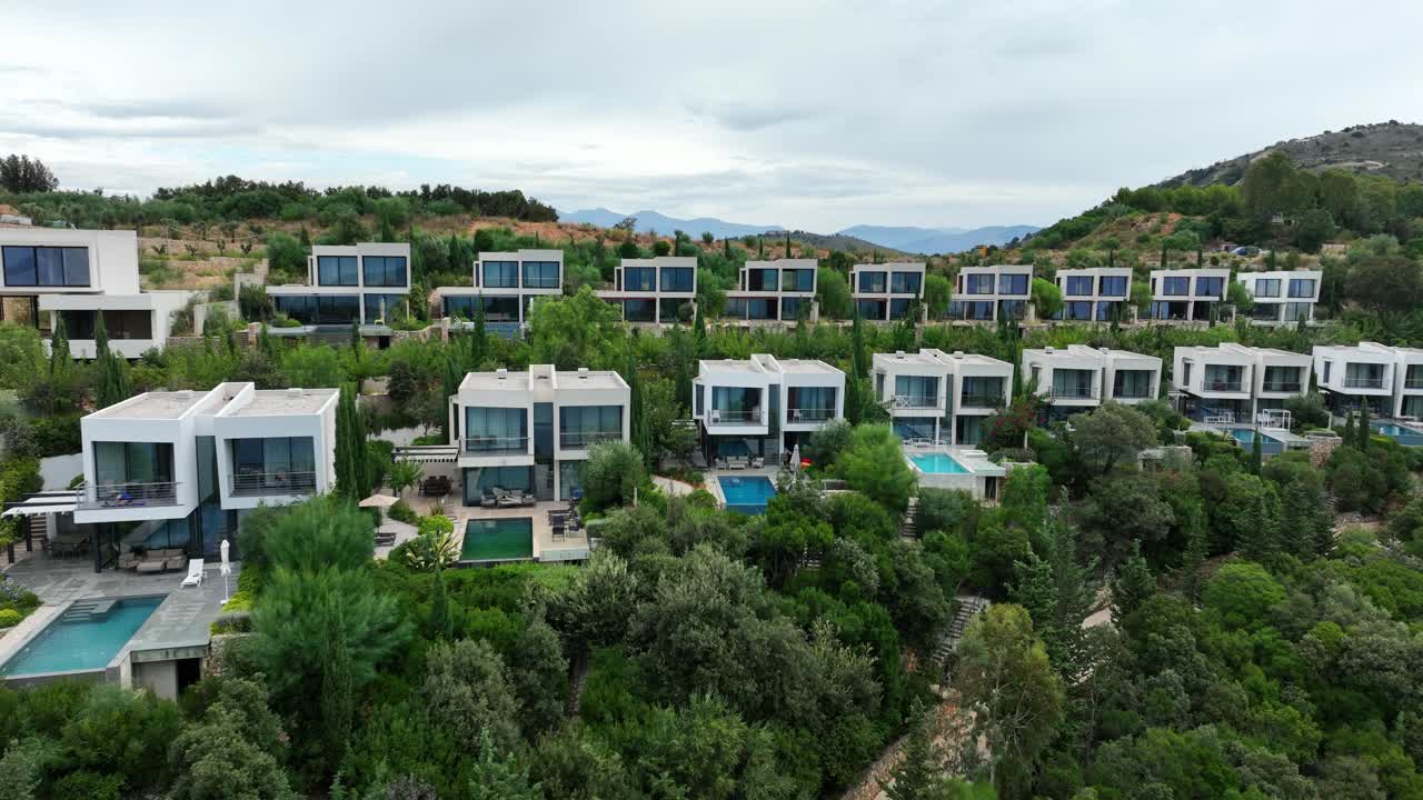 Modern buildings with pools by green hills at Sarande, Albania, aerial pan