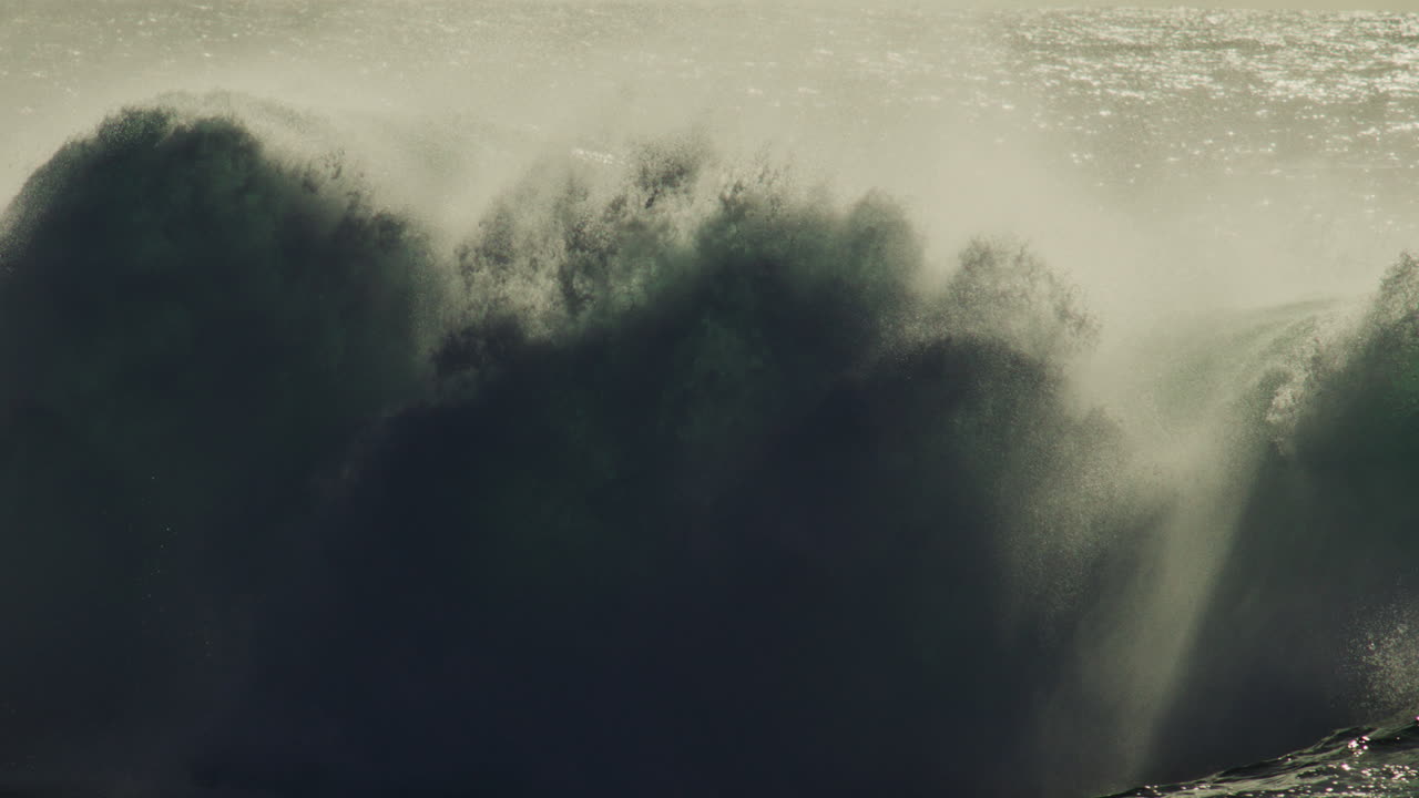 Thick mist rises from crashing wave in shadowed water during early morning slow motion