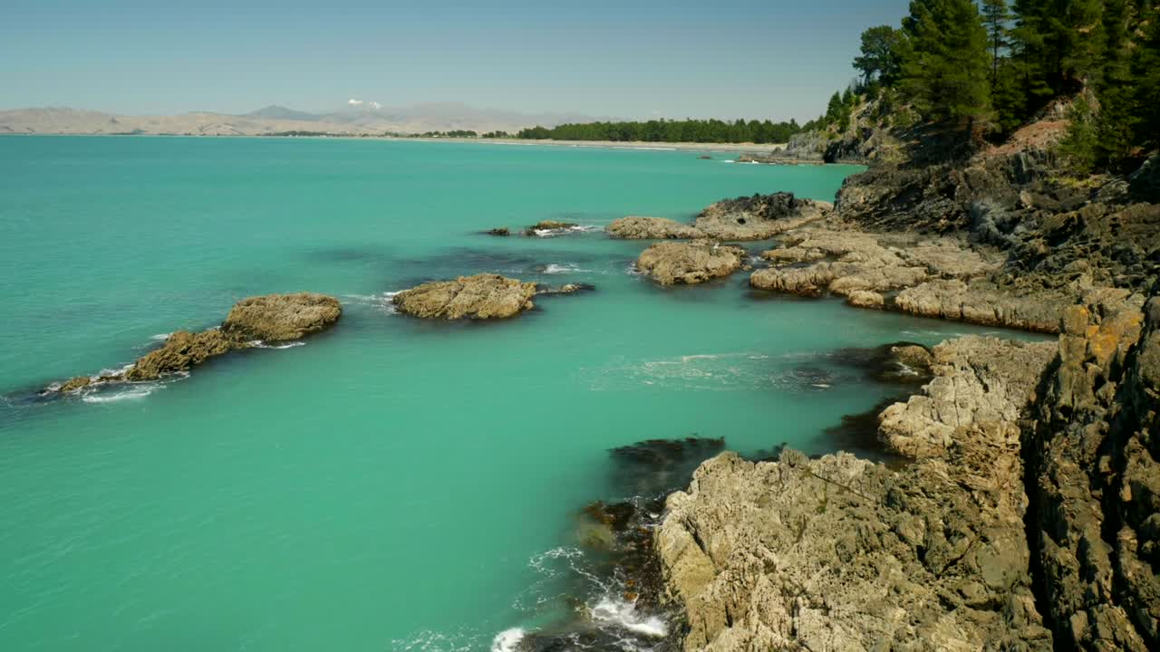 Una vista mozzafiato di una serena baia blu, incorniciata dal maestoso sfondo di montagne innevate, che crea una scena pittoresca e tranquilla