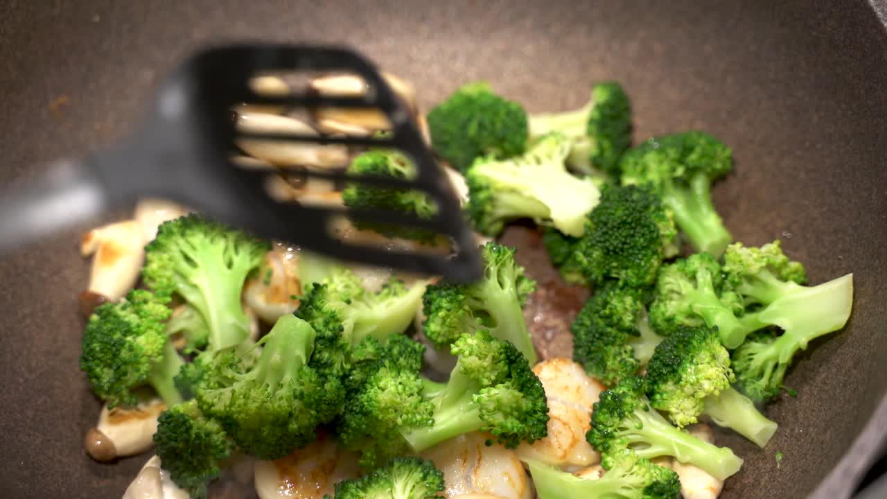 Delicious scallops, broccoli and mushrooms being fried cooked in a large pan