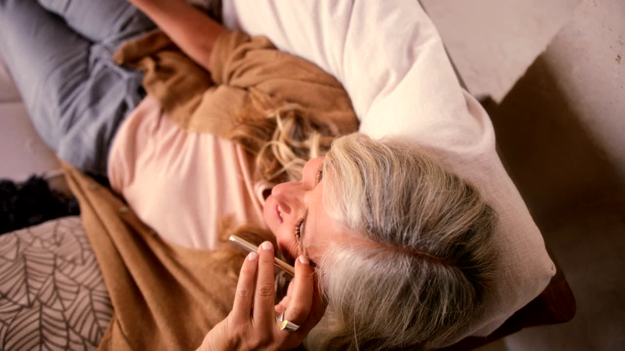 집에 있는 고령 여성이 드폰으로 얘기하고 웃고 있습니다.