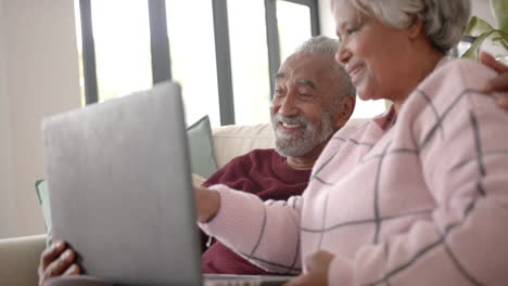 happy senior biracial couple sitting on sofa and using laptop, unaltered, in slow motion