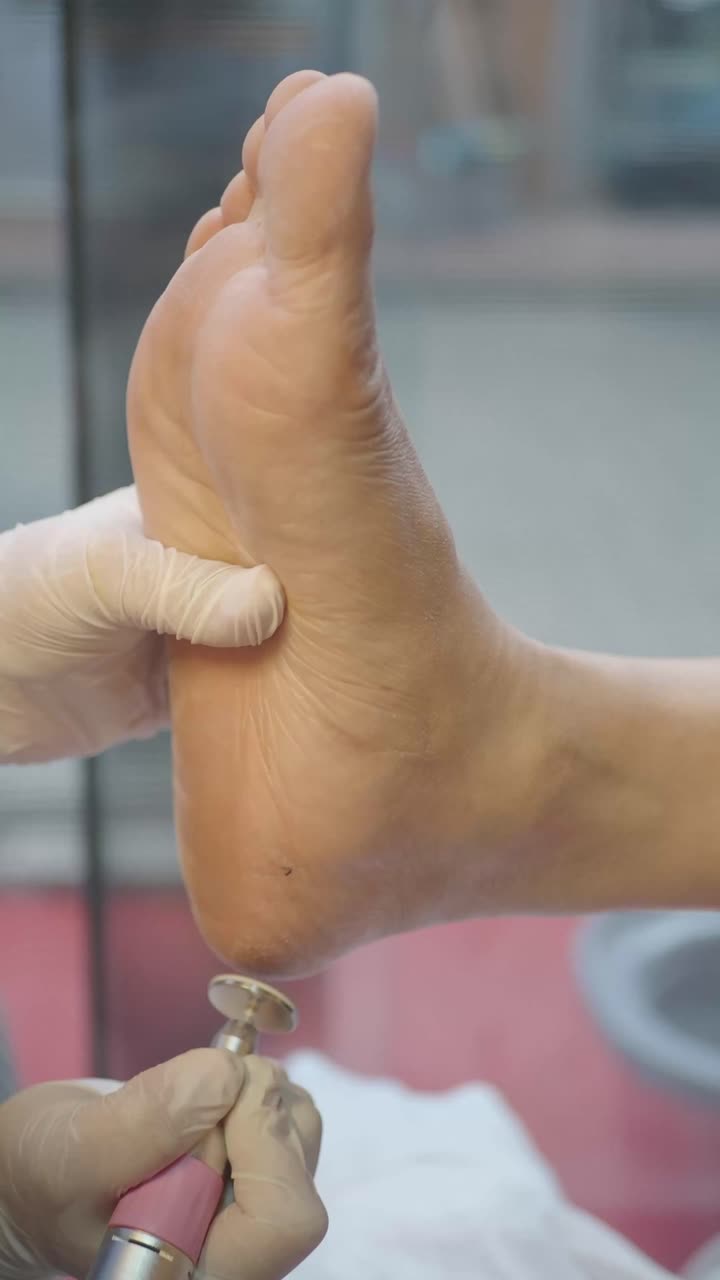 Professional Pedicurist Smoothing Client's Heel with Electric File